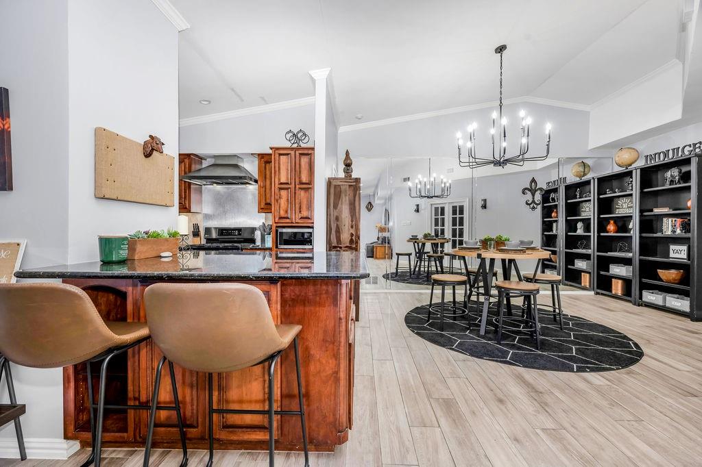 3330 Timberview Road Dallas, TX 75229 - Photo 18 of 39 Kitchen featuring light wood-type flooring, ornamental molding, wall chimney exhaust hood, vaulted ceiling, and decorative light fixtures