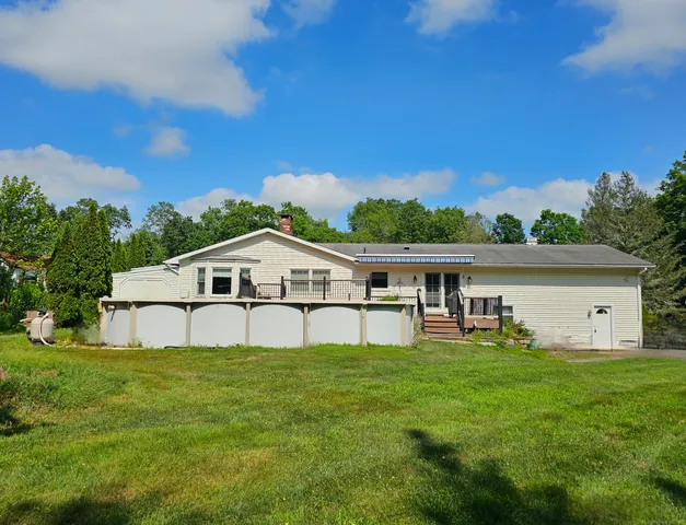 a house that is sitting in the grass with large trees and plants