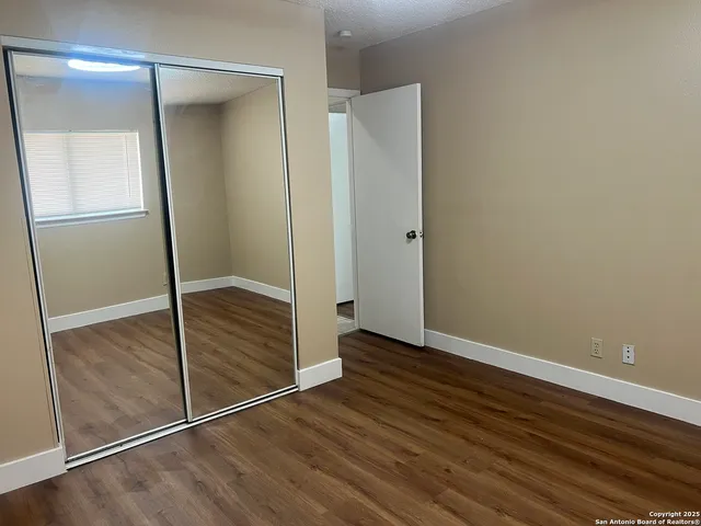 a view of an empty room with wooden floor and a mirror