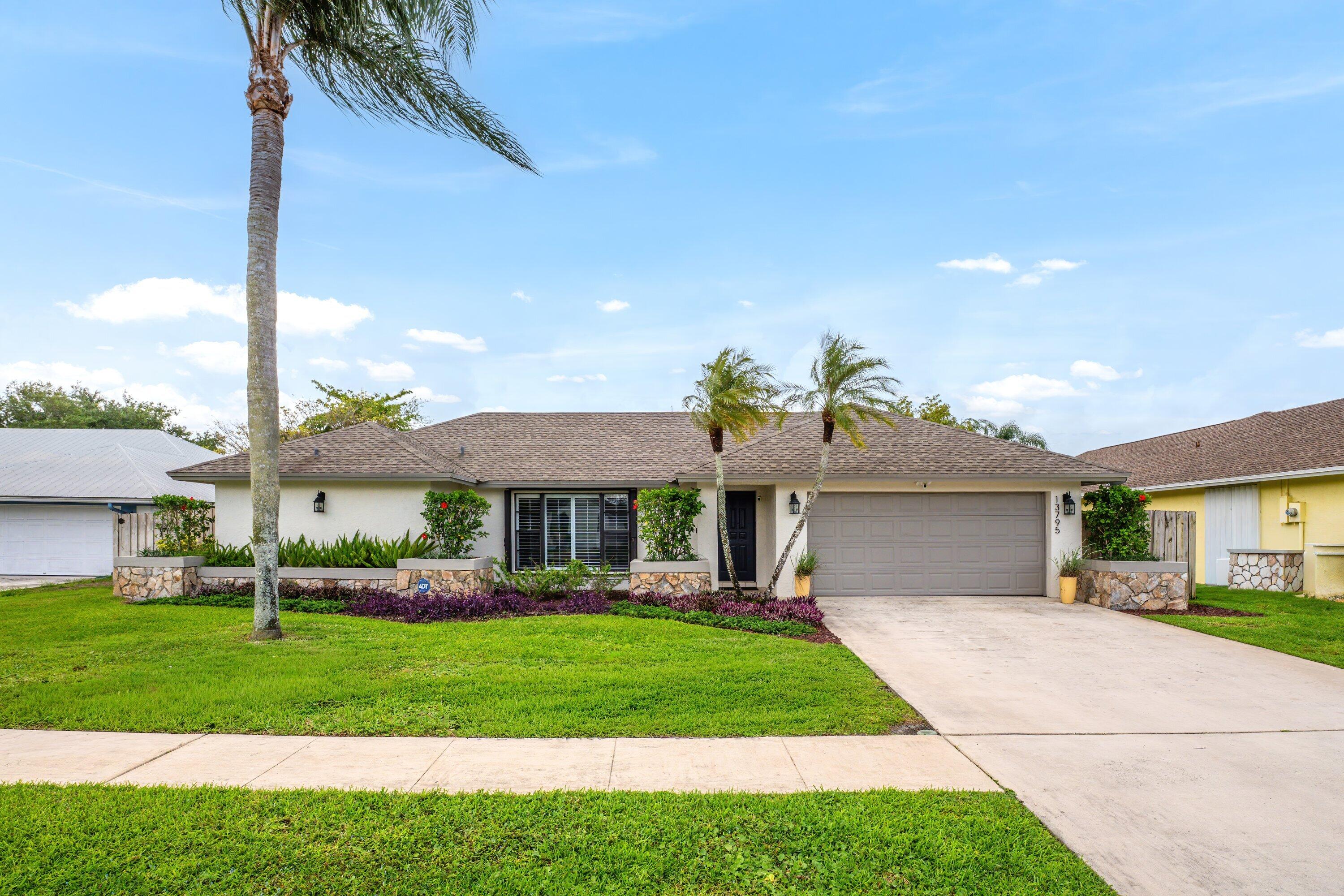 13795 Geranium Place Wellington, FL 33414 - Photo 1 of 37 a front view of a house with a garden and trees