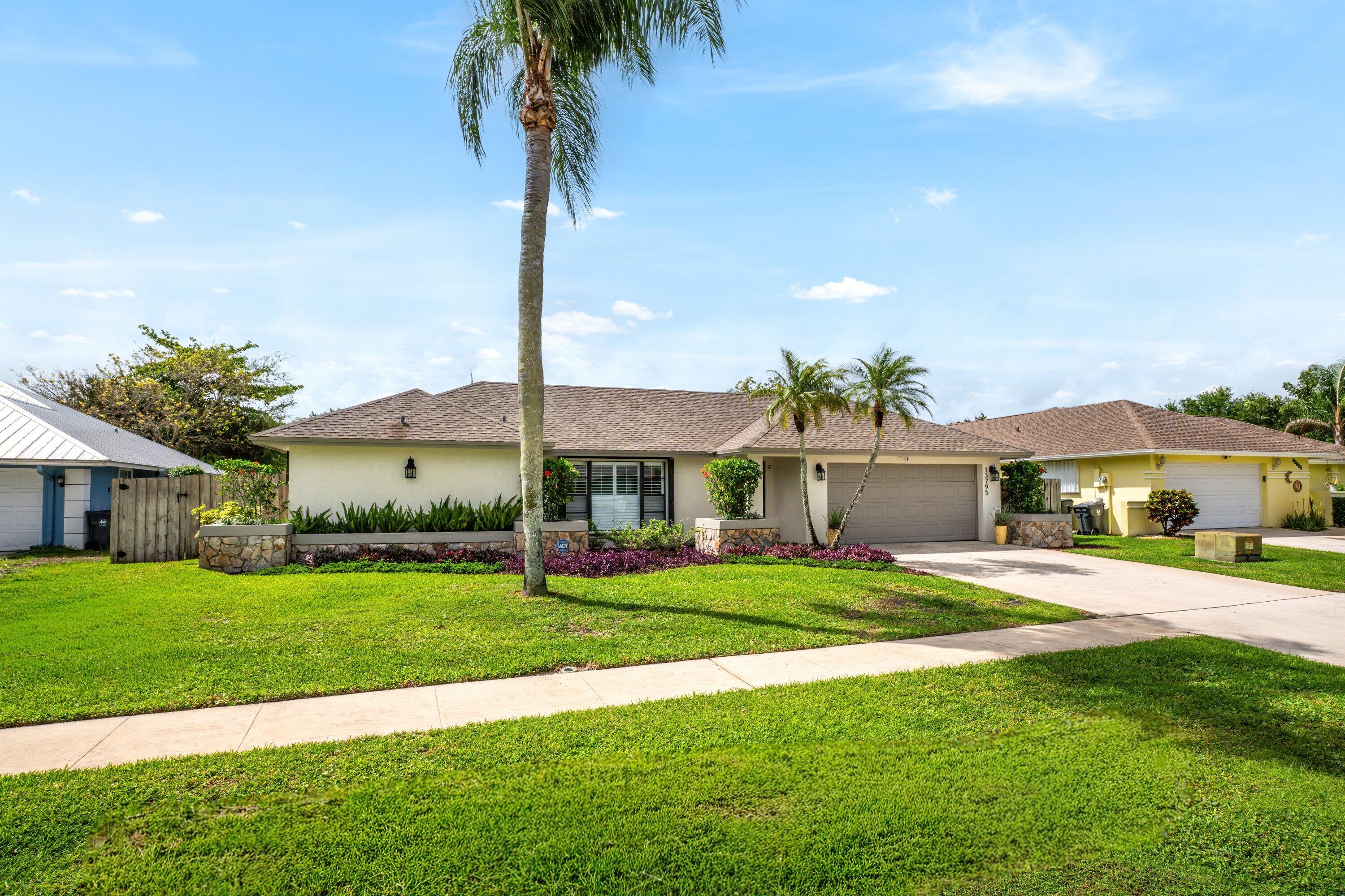 13795 Geranium Place Wellington, FL 33414 - Photo 2 of 37 a front view of a house with a garden and trees