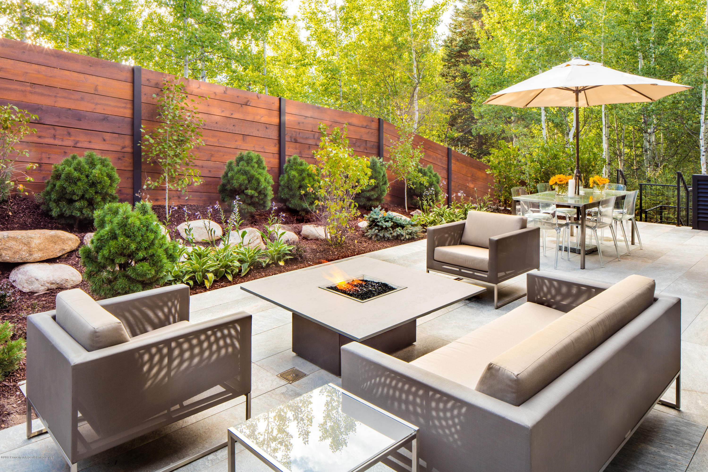 1195 Riverside Drive Aspen, CO 81611 - Photo 18 of 19 a view of a patio with couches table and chairs under an umbrella with a small garden