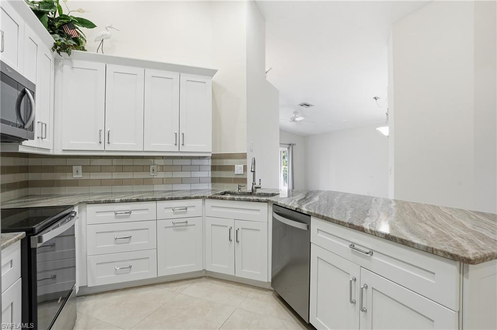 3724 Stone Way Estero, FL 33928 - Photo 16 of 35 Kitchen with light stone counters, appliances with stainless steel finishes, white cabinetry, backsplash, and a peninsula