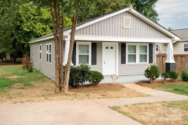 a view of a house with a yard plants and large tree
