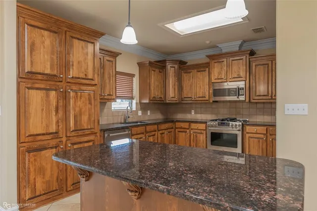 a kitchen with stainless steel appliances granite countertop a refrigerator a sink dishwasher a stove with wooden cabinets and floor