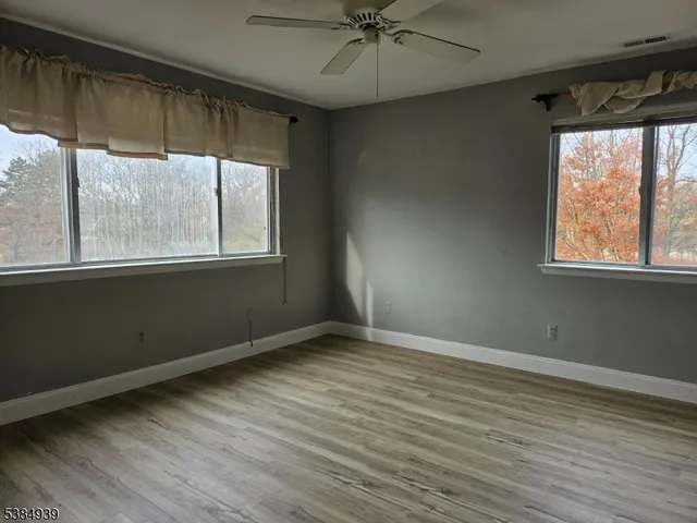 an empty room with wooden floor fan and windows