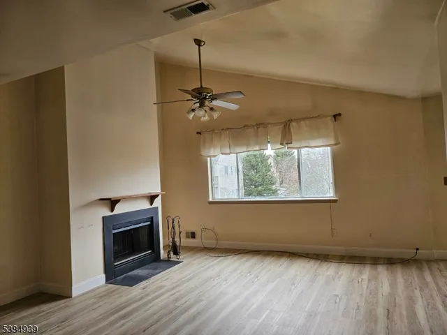 a view of empty room with wooden floor fireplace and fan