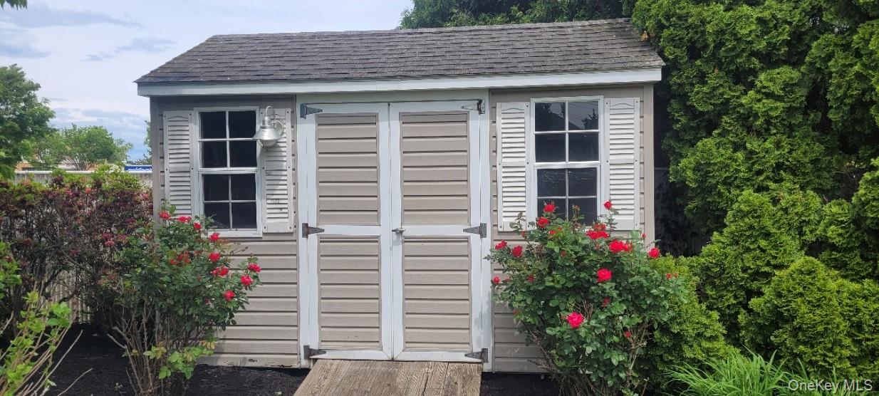 312 Riley Avenue Calverton, NY 11933 - Photo 24 of 30 Exterior storage shed with vinyl siding, shingled roof, double entry doors, window with louvered shutters, and exterior electric wall-mounted lighting