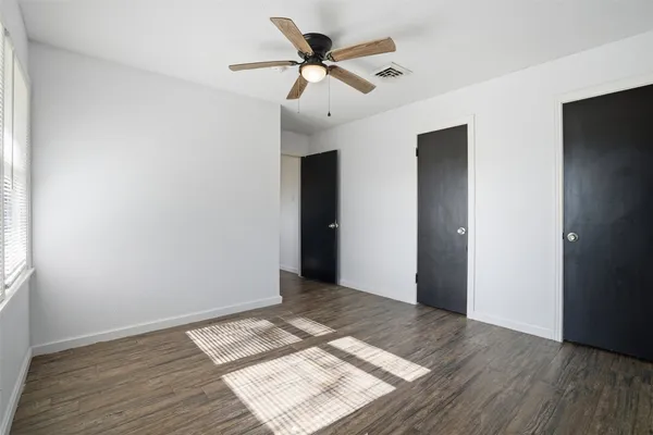 a view of an empty room with wooden floor and a ceiling fan