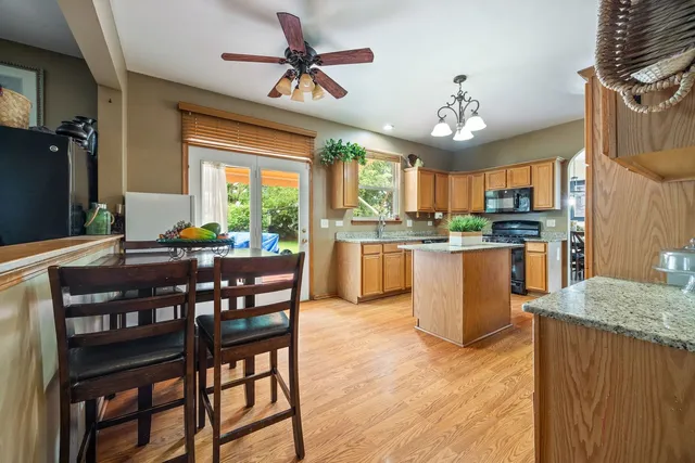 a open kitchen with stainless steel appliances granite countertop a stove top oven a refrigerator a sink dishwasher a dining table and chairs with wooden floor