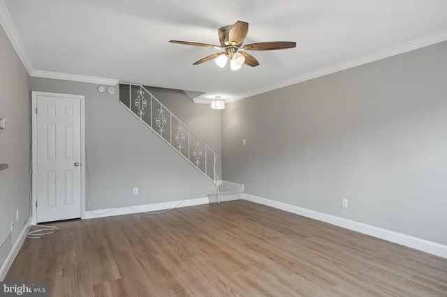 a view of an empty room with wooden floor and a ceiling fan