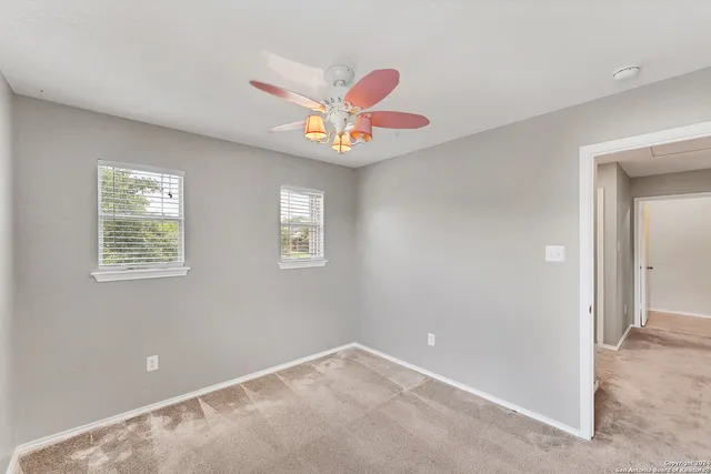 an empty room with a chandelier fan and windows