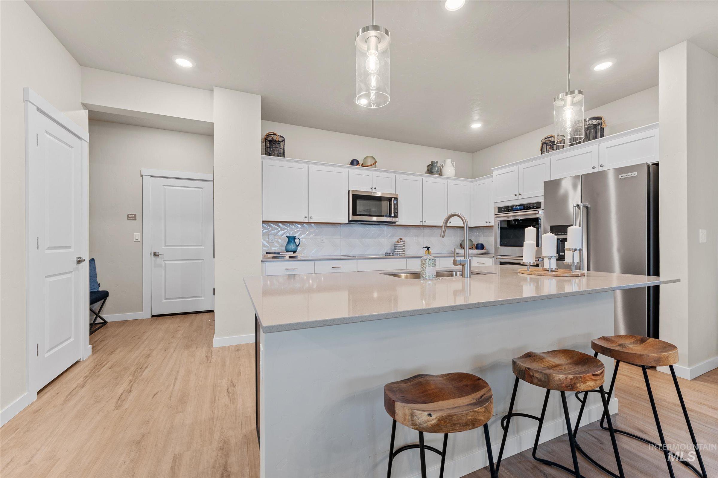 4149 South Colditz Way Meridian, ID 83642 - Photo 12 of 42 Kitchen with decorative backsplash, light wood-type flooring, white cabinets, pendant lighting, and a breakfast bar