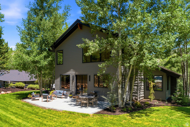 3027 Homestead Road Park City, UT 84098 - Photo 59 of 62 Modern architectural design featuring a spacious concrete patio, a manicured lawn, abundant mature trees, and a dark-toned exterior with large windows and a glass slider
