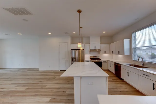 a kitchen with stainless steel appliances kitchen island granite countertop a stove a sink a refrigerator and white cabinets with wooden floor