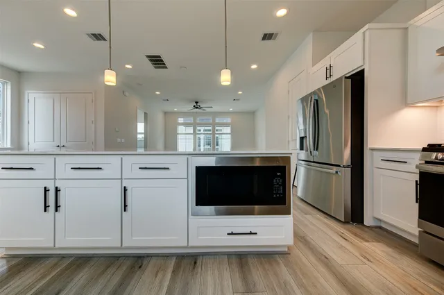 a kitchen with stainless steel appliances kitchen island granite countertop a refrigerator a oven a sink and white cabinets with wooden floor