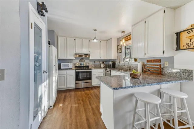 a kitchen with stainless steel appliances granite countertop a refrigerator a stove a sink and white cabinets with wooden floor