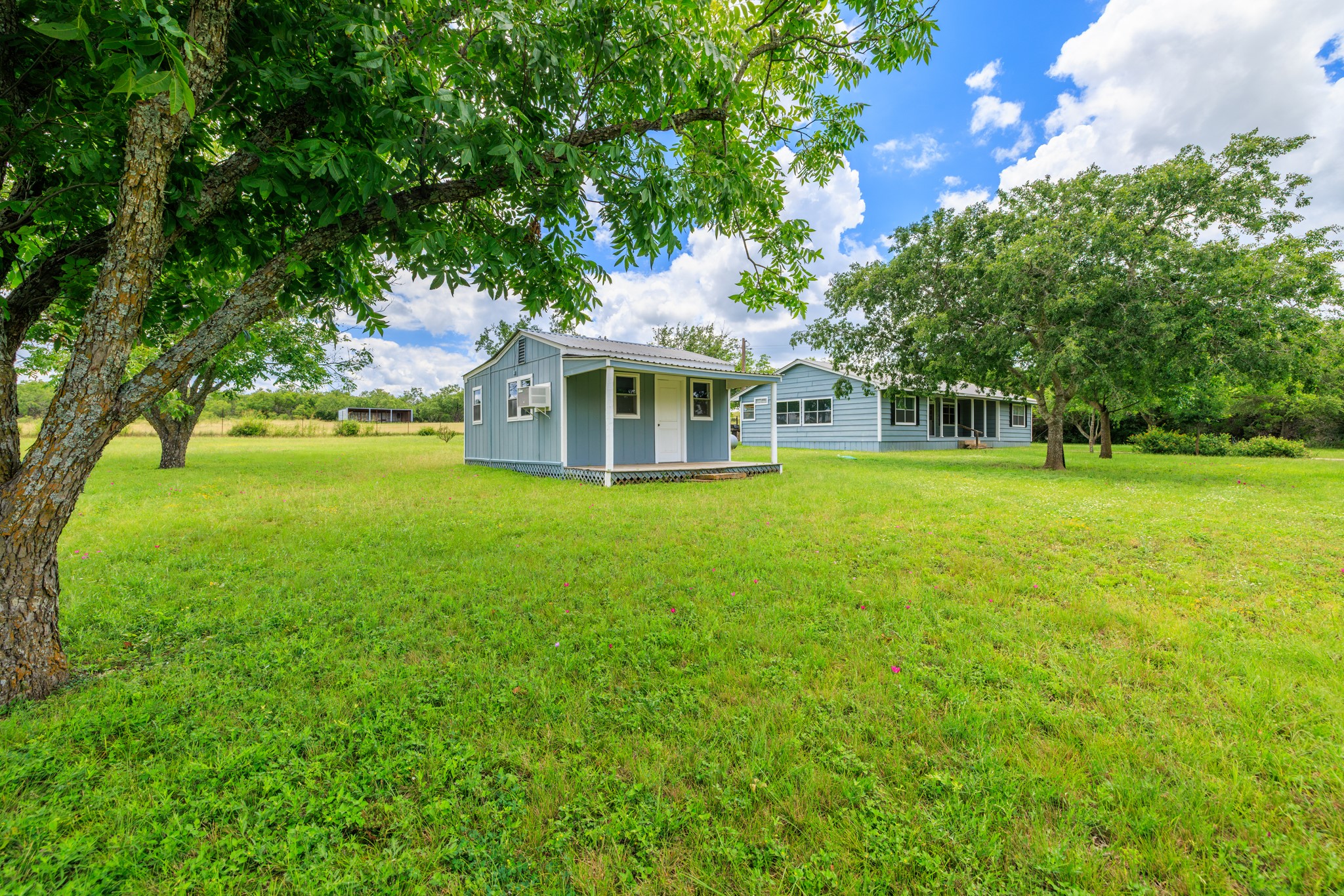 341 River View Road Fredericksburg, TX 78624 - Photo 25 of 40 Mature shade trees frame a sprawling grassy lawn with multiple outbuildings under blue skies.