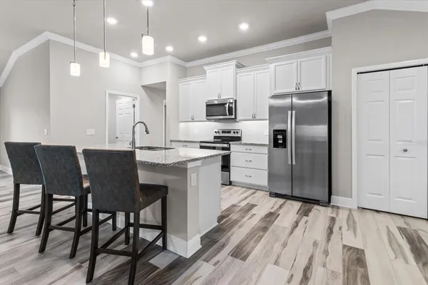 a kitchen with stainless steel appliances a refrigerator a stove a sink a dining table and chairs with wooden floor