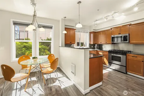 a kitchen with stainless steel appliances granite countertop a stove top oven a sink dishwasher a dining table and chairs with wooden floor