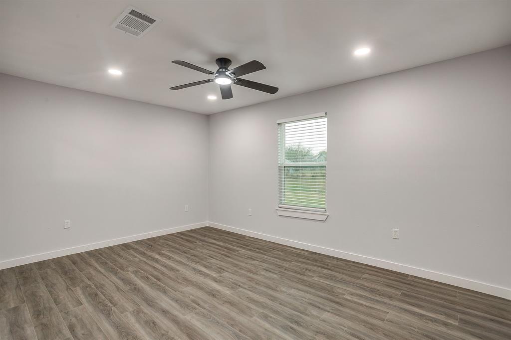 122 Kentucky Street Walnut Springs, TX 76690 - Photo 8 of 18 an empty room with wooden floor fan and windows
