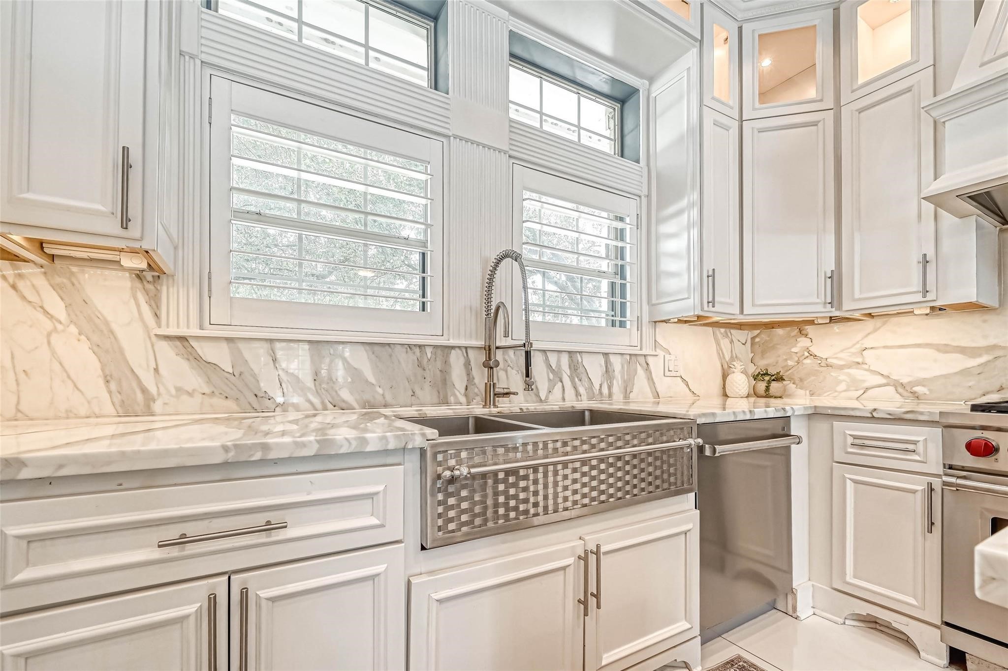 263 Wood Loop Street Houston, TX 77015 - Photo 28 of 45 This kitchen features elegant white cabinetry, a marble backsplash, and a large farmhouse sink under a window with shutters. The space is bright and modern, offering ample storage and a stylish, functional design.