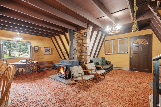 8505 South Snake Crk Road Salt Lake City, UT 84121 - Photo 8 of 67 A-frame interior featuring a central stone-clad wood-burning stove, exposed ceiling beams, wood-paneled walls, and an arched top entry door