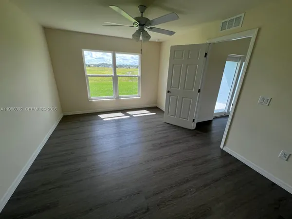 an empty room with wooden floor a ceiling fan and windows