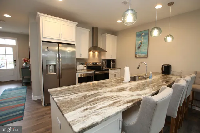 a kitchen with stainless steel appliances granite countertop a refrigerator a sink dishwasher a stove and white cabinets with wooden floor