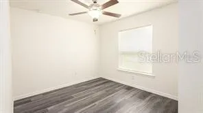 an empty room with wooden floor fan and windows