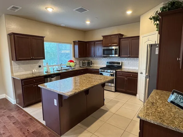 a kitchen with stainless steel appliances granite countertop wooden cabinets a sink a stove a refrigerator and a oven