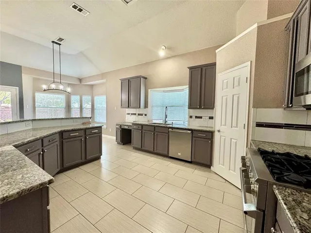 a large kitchen with stainless steel appliances granite countertop a stove a sink dishwasher a refrigerator and white cabinets with wooden floor