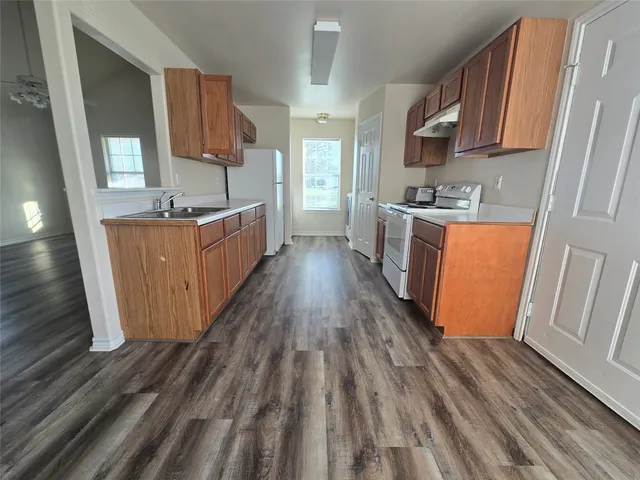 a kitchen with wooden floors wooden cabinets a sink a stove a chimney and a window