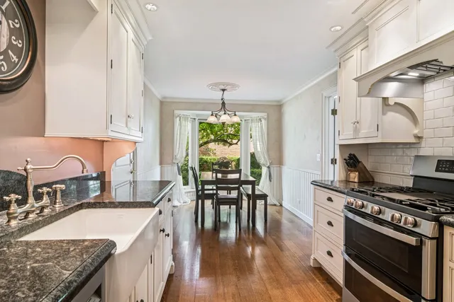 a kitchen with stainless steel appliances granite countertop a stove top oven a sink a dining table and chairs with wooden floor