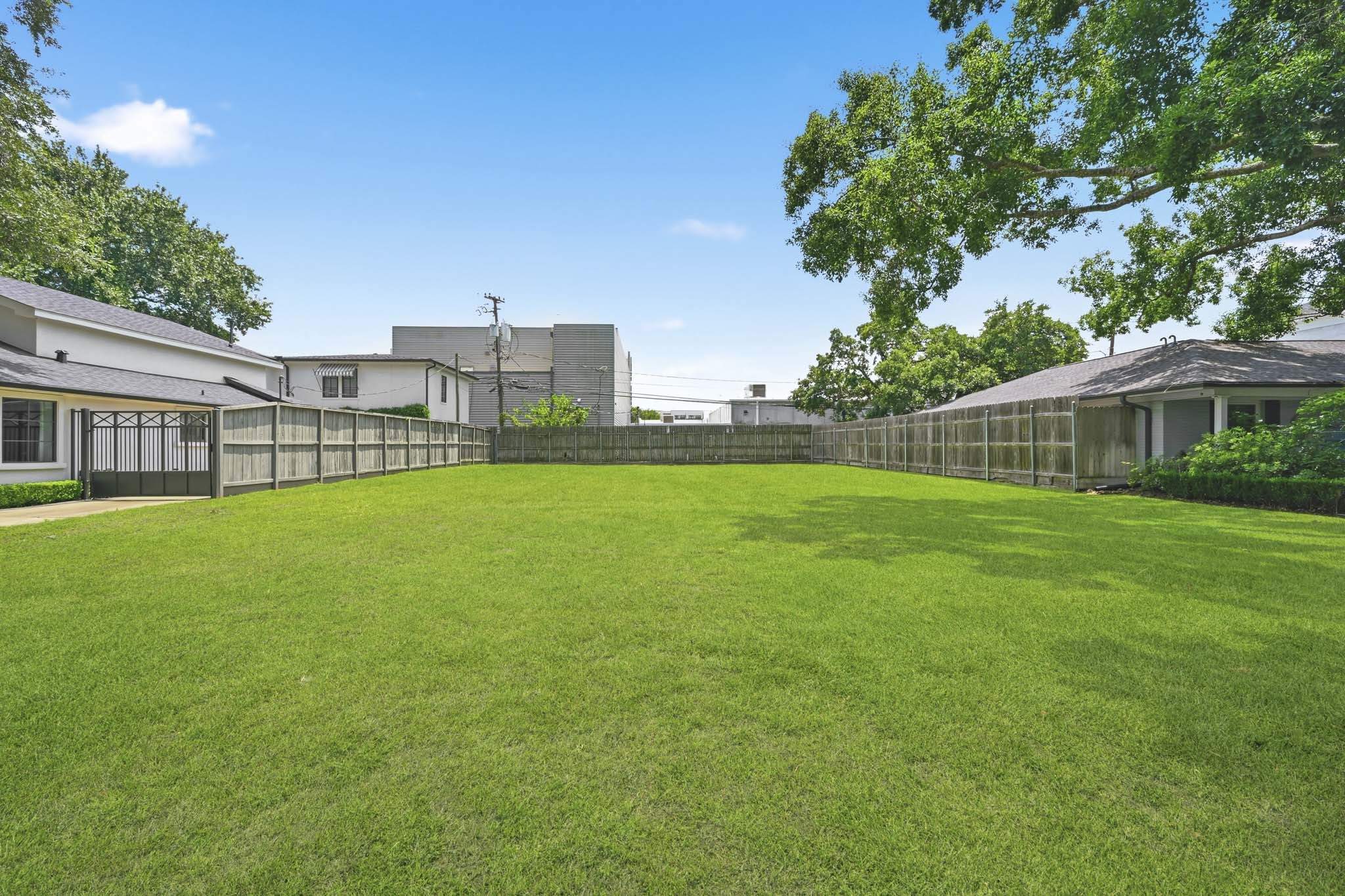 4227 Markham Street Houston, TX 77027 - Photo 7 of 7 This photo showcases a spacious, fenced backyard with lush green grass, bordered by neighboring homes and shaded by mature trees, perfect for outdoor activities and privacy.