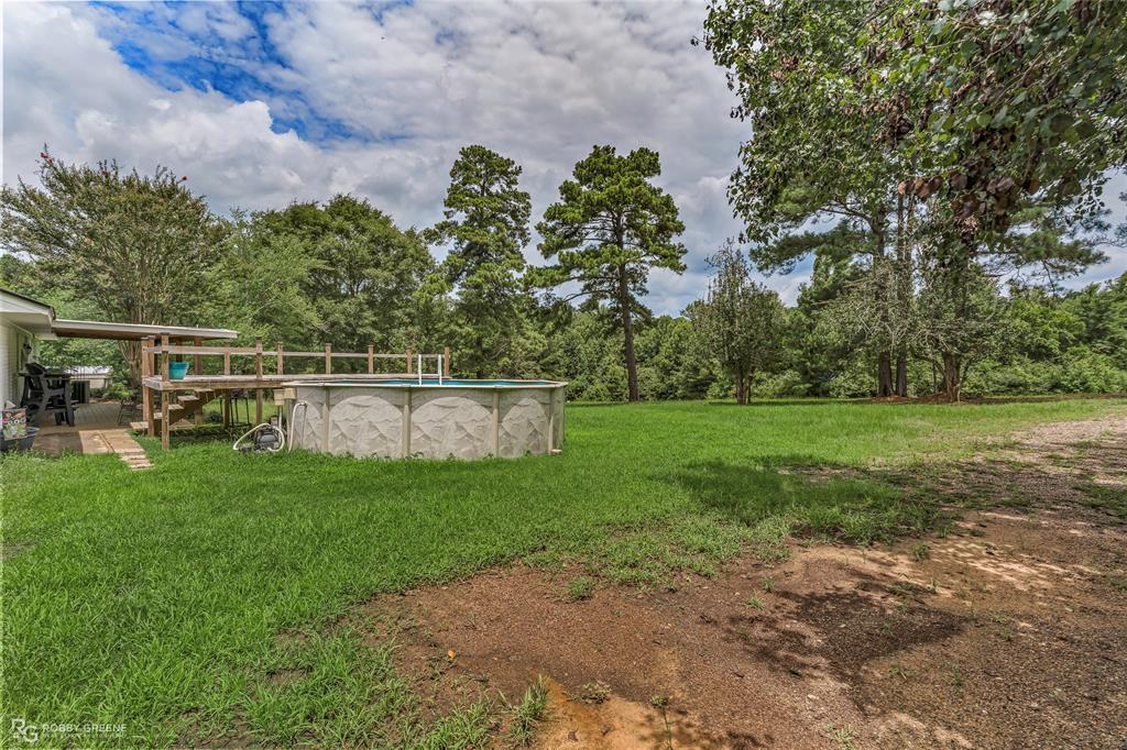 1426 Caney Lake Road Minden, LA 71055 - Photo 27 of 36 Expansive rear yard featuring an above-ground pool with a surrounding wood deck, a covered patio area, and mature trees providing natural screening