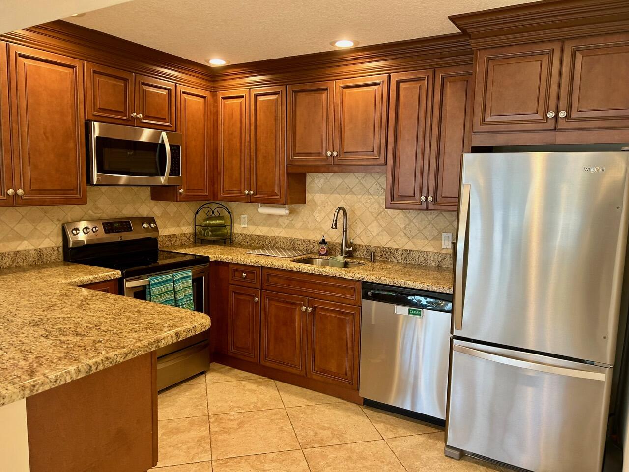 1 Southeast Turtle Creek Drive, Unit B Jupiter, FL 33469 - Photo 29 of 31 a kitchen with stainless steel appliances granite countertop a refrigerator stove top oven and sink