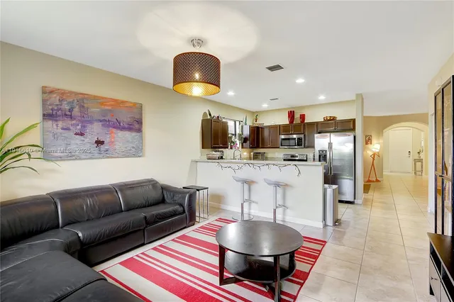 a living room kitchen with stainless steel appliances kitchen island granite countertop a refrigerator a stove a dining table and chairs