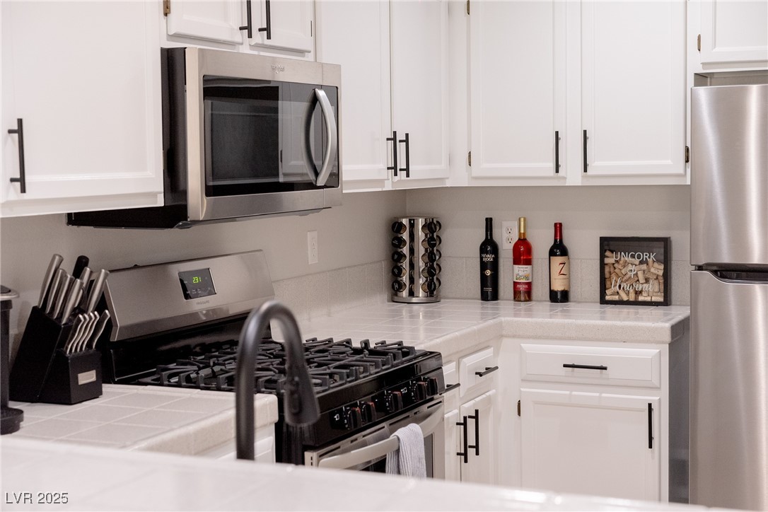 7950 West Flamingo Road, Unit 1173 Las Vegas, NV 89147 - Photo 15 of 31 Kitchen with appliances with stainless steel finishes, white cabinets, and tile countertops