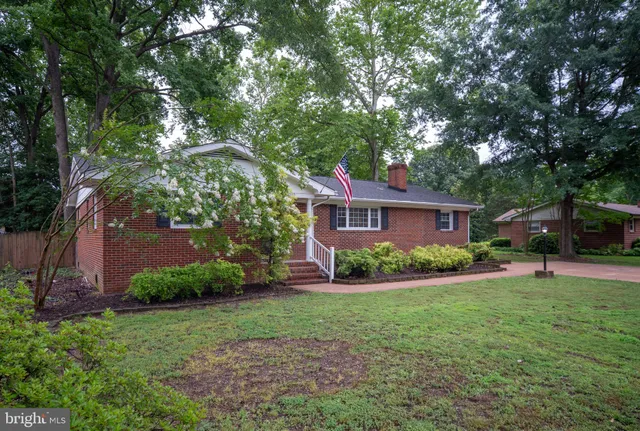 a view of a brick house with a big yard plants and large trees