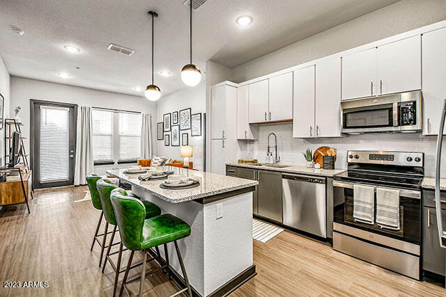 26800 North 27th Avenue, Unit B2 Phoenix, AZ 85085 - Photo 4 of 10 a kitchen with stainless steel appliances granite countertop a stove a sink a microwave a refrigerator a dining table and chairs with wooden floor