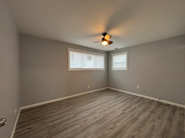 an empty room with wooden floor chandelier fan and windows
