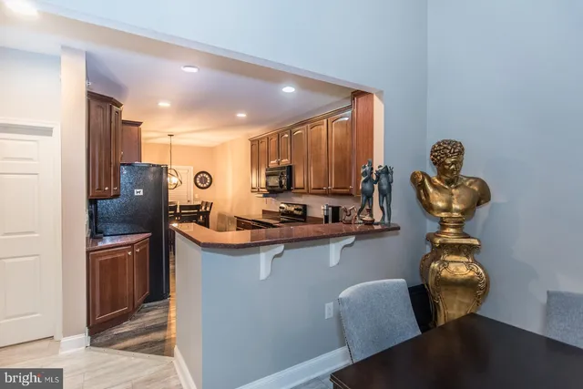 a kitchen with stainless steel appliances granite countertop a refrigerator a stove a sink a dining table and chairs with wooden floor