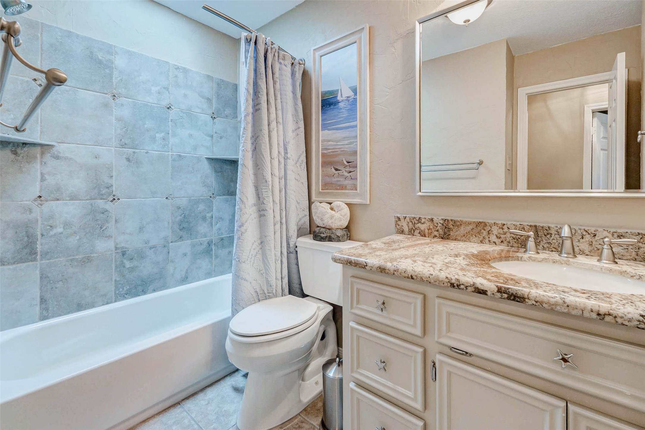 15811 Spring Forest Drive Houston, TX 77059 - Photo 16 of 27 This elegant bathroom features a beautifully tiled shower, a stylish granite countertop, and charming coastal artwork, creating a serene and inviting space.