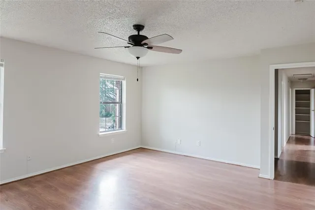 a view of an empty room with wooden floor and a ceiling fan