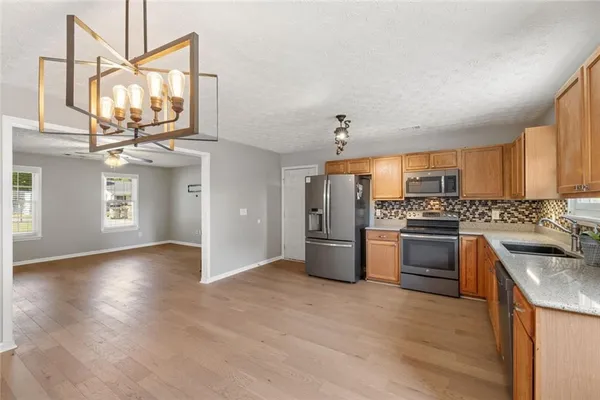 a kitchen with stainless steel appliances granite countertop a refrigerator a sink dishwasher a stove with wooden cabinets and floors