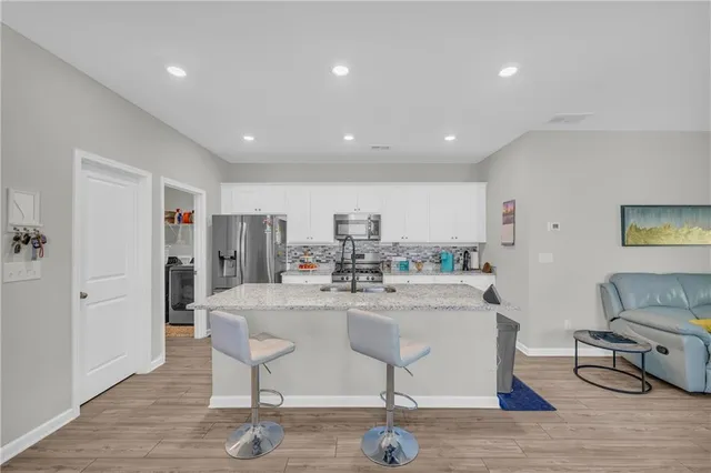 a living room with stainless steel appliances granite countertop furniture a refrigerator a kitchen island a stove and a refrigerator with wooden floor