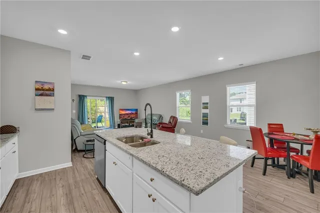 a kitchen with stainless steel appliances granite countertop a stove a sink dishwasher a refrigerator and white cabinets with wooden floor