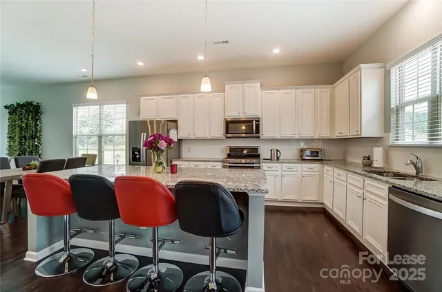 a kitchen with stainless steel appliances granite countertop a stove top oven a sink dishwasher a dining table and chairs with wooden floor