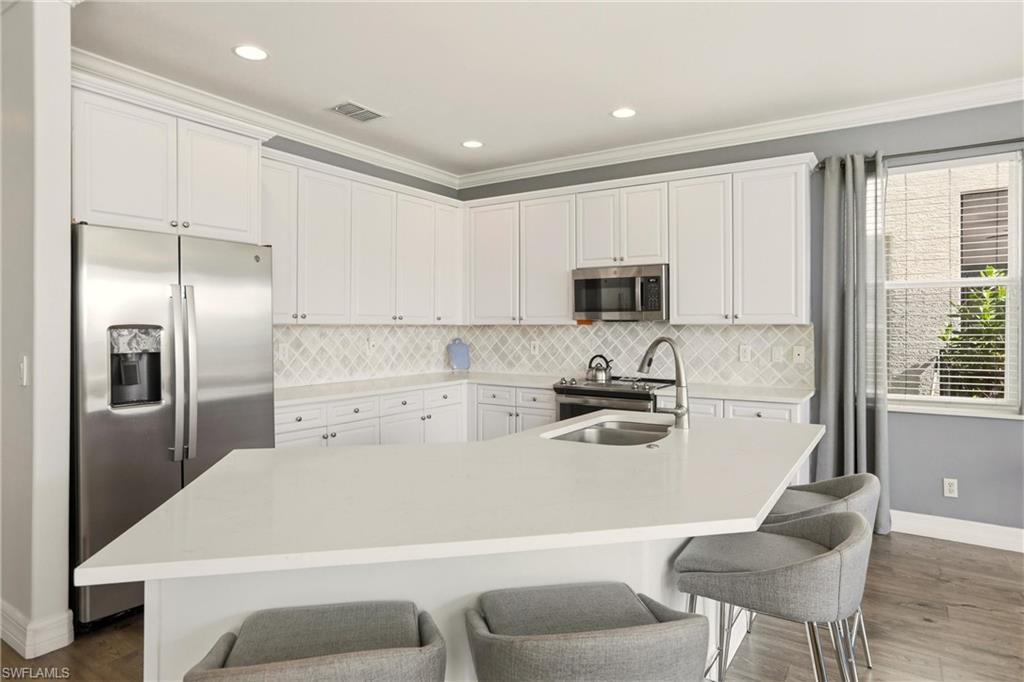 2150 Khasia Point Naples, FL 34119 - Photo 9 of 42 a kitchen with stainless steel appliances a refrigerator a stove a sink dishwasher and white cabinets with wooden floor